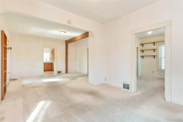 empty room featuring carpet, visible vents, and arched walkways