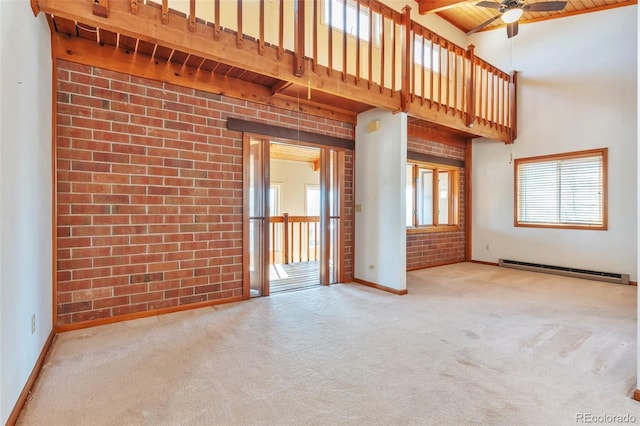 empty room with carpet, a towering ceiling, baseboard heating, brick wall, and wooden ceiling