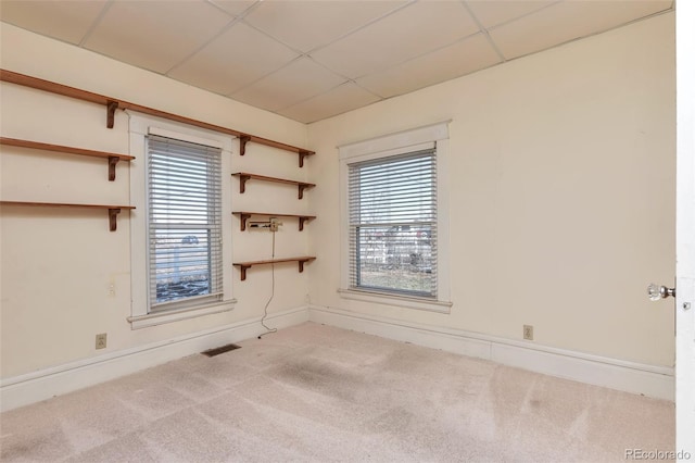 carpeted empty room with visible vents, a paneled ceiling, and baseboards