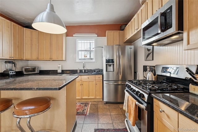 34 W Maple Ave, Denver, CO 80223 - kitchen with appliances with stainless steel finishes, light brown cabinetry, a breakfast bar, dark stone countertops, and pendant lighting