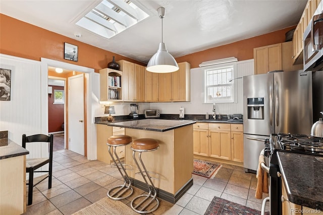 34 W Maple Ave, Denver, CO 80223 - kitchen featuring stainless steel appliances, light brown cabinets, dark countertops, and a kitchen breakfast bar