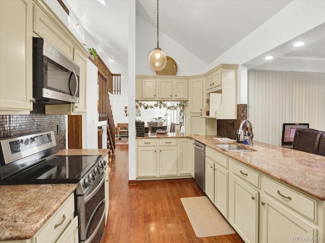 3596 S Telluride Way, Aurora, CO 80013 - kitchen featuring appliances with stainless steel finishes, cream cabinetry, a peninsula, backsplash, and vaulted ceiling