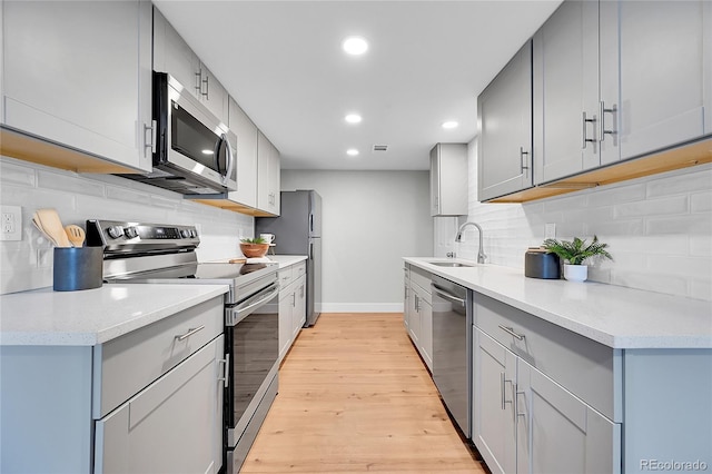 kitchen featuring light wood finished floors, baseboards, appliances with stainless steel finishes, a sink, and gray cabinets