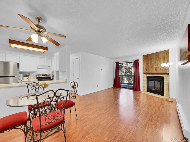 kitchen with white cabinets, light hardwood / wood-style flooring, a brick fireplace, a baseboard radiator, and stainless steel appliances