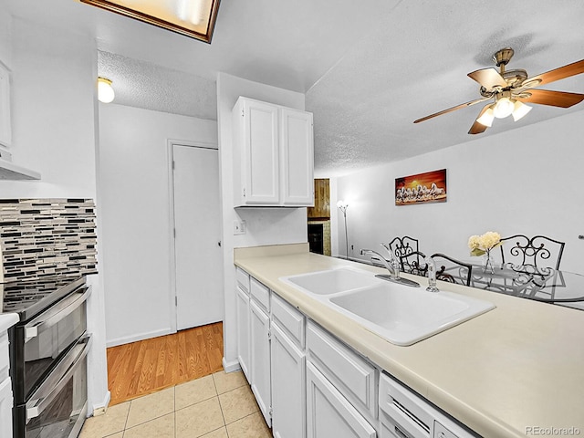 kitchen featuring sink, tasteful backsplash, light tile patterned flooring, stainless steel range oven, and white cabinetry