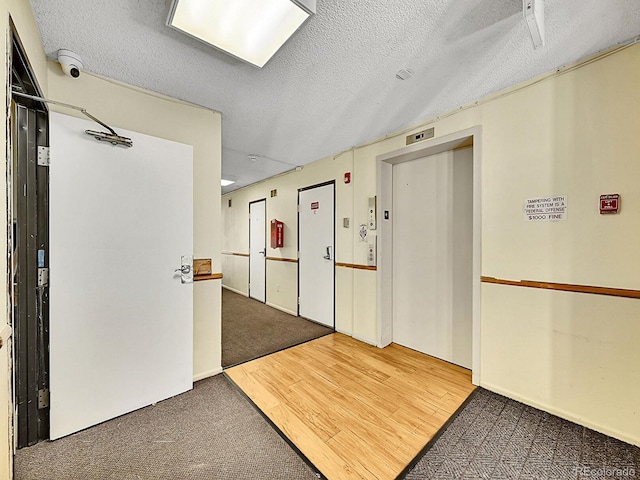 hallway with a textured ceiling, elevator, and hardwood / wood-style flooring