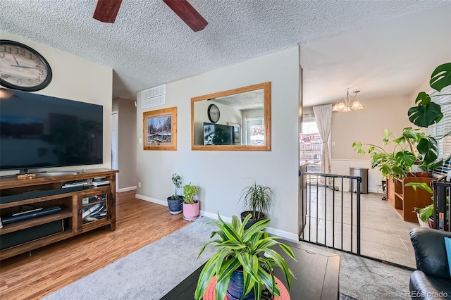 living room with ceiling fan with notable chandelier, light hardwood / wood-style flooring, and a textured ceiling