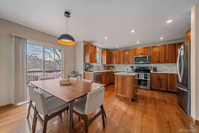 kitchen featuring brown cabinets, stainless steel appliances, light countertops, a sink, and light wood-type flooring