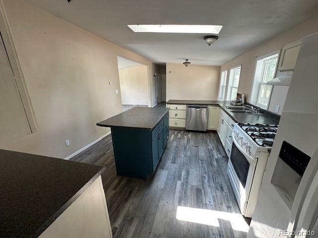 13193 E US Highway 160, Alamosa, CO 81101 - kitchen with dishwasher, white gas range oven, dark countertops, a skylight, and dark wood finished floors