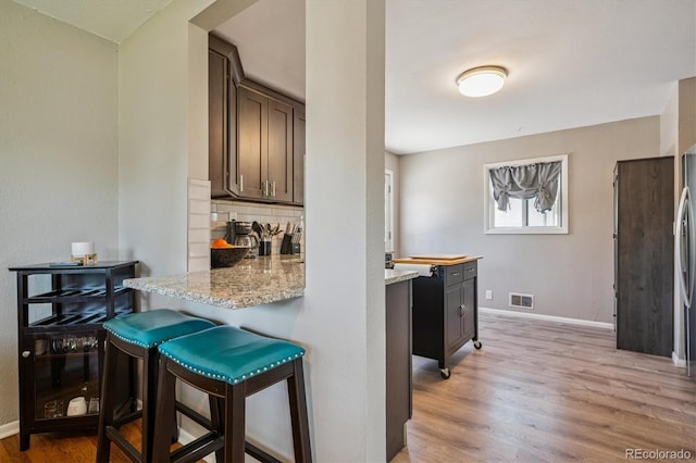 3995 Nelson St, Wheat Ridge, CO 80033 - kitchen featuring light wood-style flooring, tasteful backsplash, a kitchen breakfast bar, light stone counters, and a peninsula