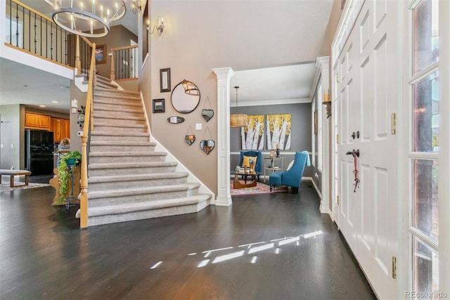 entryway featuring crown molding, a chandelier, dark hardwood / wood-style flooring, and ornate columns