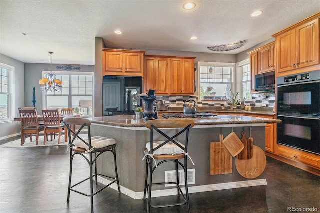 kitchen featuring a kitchen island, an inviting chandelier, decorative light fixtures, black appliances, and a kitchen bar