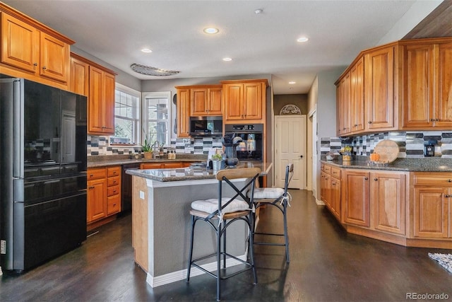 kitchen featuring a breakfast bar area, black appliances, a center island, dark wood-type flooring, and decorative backsplash