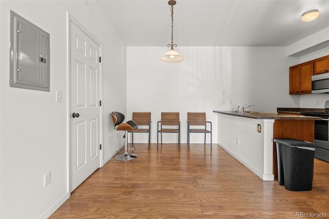 kitchen featuring electric panel, appliances with stainless steel finishes, light wood-style flooring, dark countertops, and brown cabinetry