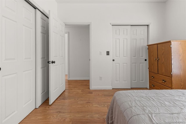 bedroom featuring light wood finished floors, baseboards, and multiple closets