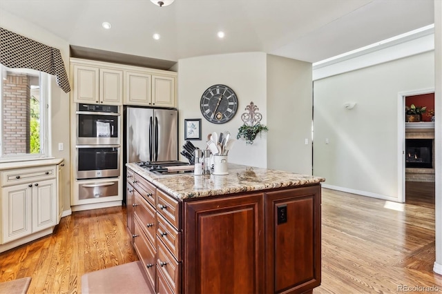 kitchen with a warming drawer, light stone counters, light wood-type flooring, and stainless steel appliances