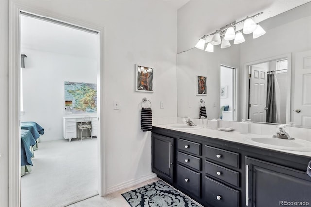 full bath featuring double vanity, connected bathroom, baseboards, and a sink