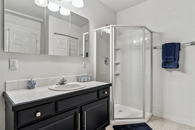 full bath featuring a shower stall, vanity, baseboards, and a textured wall