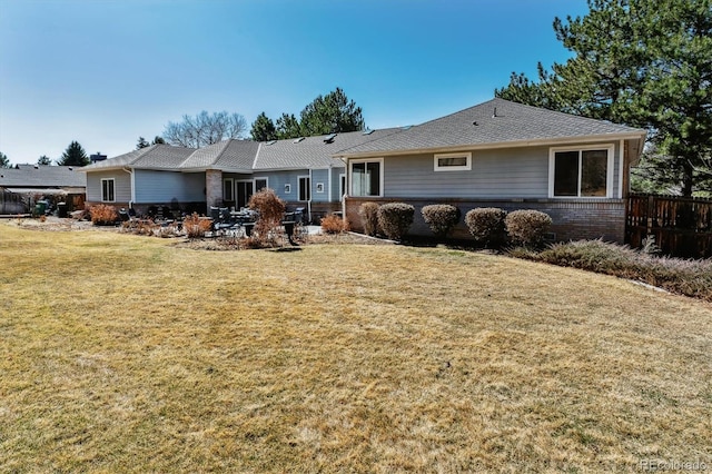 back of property featuring brick siding, a lawn, fence, and roof with shingles