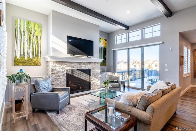 living room with beam ceiling, hardwood / wood-style flooring, and a stone fireplace