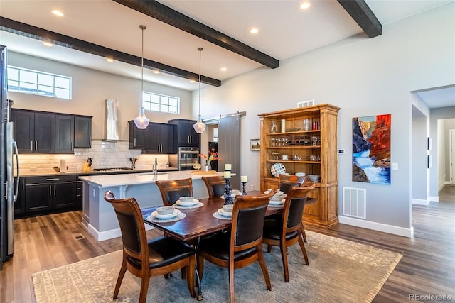 dining room with a towering ceiling, hardwood / wood-style floors, a barn door, and beam ceiling