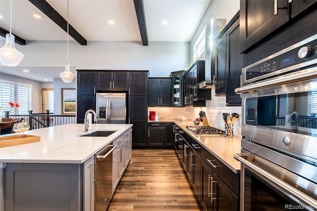 kitchen with a kitchen island with sink, appliances with stainless steel finishes, beam ceiling, sink, and decorative light fixtures