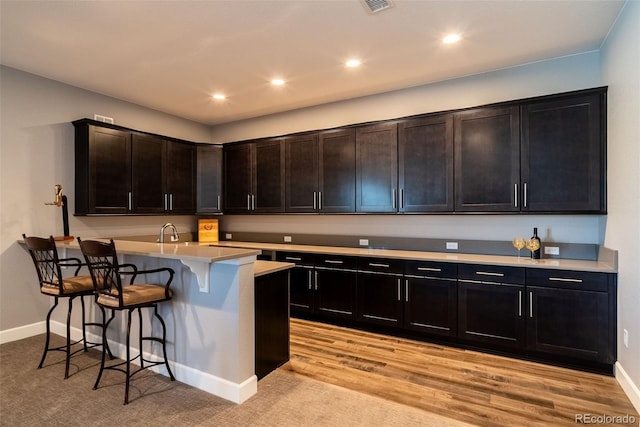 kitchen featuring sink, light hardwood / wood-style floors, a breakfast bar, and dark brown cabinetry