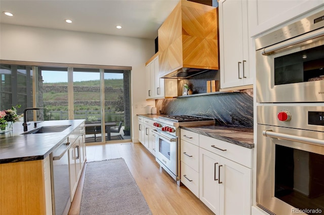 3436 W 154th Ave, Broomfield, CO 80023 - kitchen with stainless steel appliances, premium range hood, dark countertops, light wood-style floors, and recessed lighting