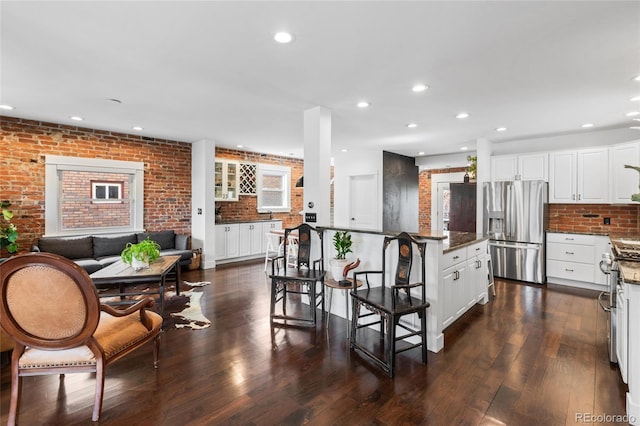449 S Humboldt St, Denver, CO 80209 - kitchen with stainless steel appliances, brick wall, a kitchen bar, white cabinetry, and dark wood finished floors