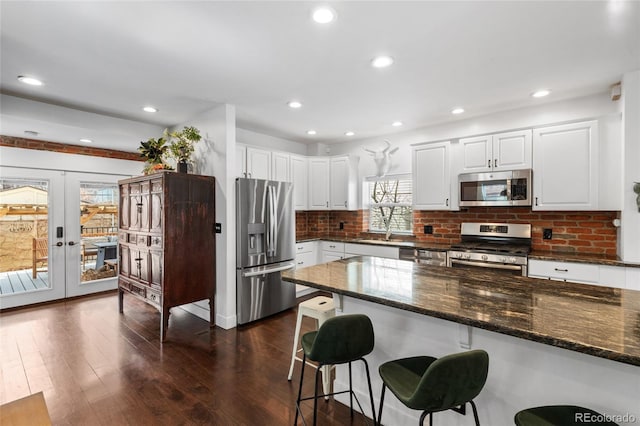 449 S Humboldt St, Denver, CO 80209 - kitchen featuring appliances with stainless steel finishes, a kitchen bar, dark wood-style flooring, white cabinetry, and tasteful backsplash