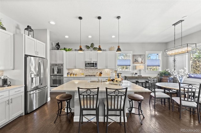 kitchen with white cabinetry, appliances with stainless steel finishes, a center island with sink, and hanging light fixtures