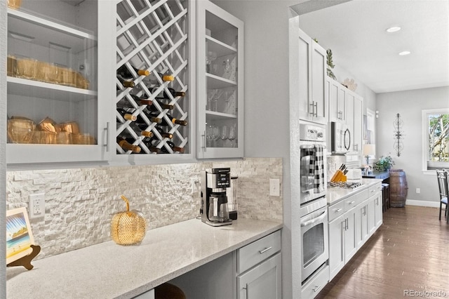 kitchen featuring light stone countertops, appliances with stainless steel finishes, backsplash, and dark hardwood / wood-style flooring