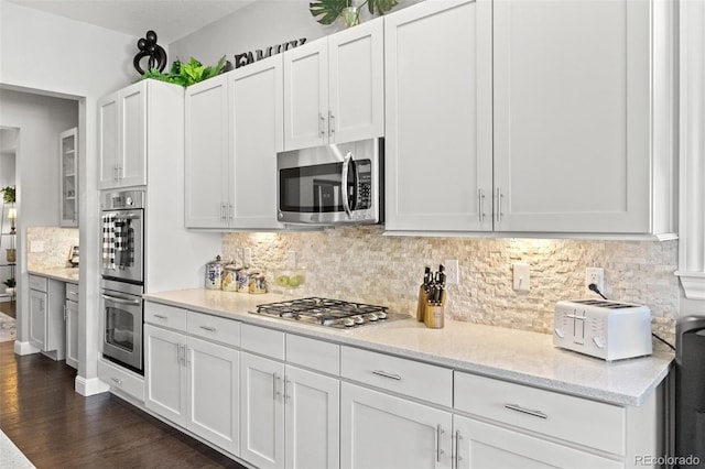 kitchen featuring backsplash, appliances with stainless steel finishes, dark hardwood / wood-style flooring, white cabinetry, and light stone counters