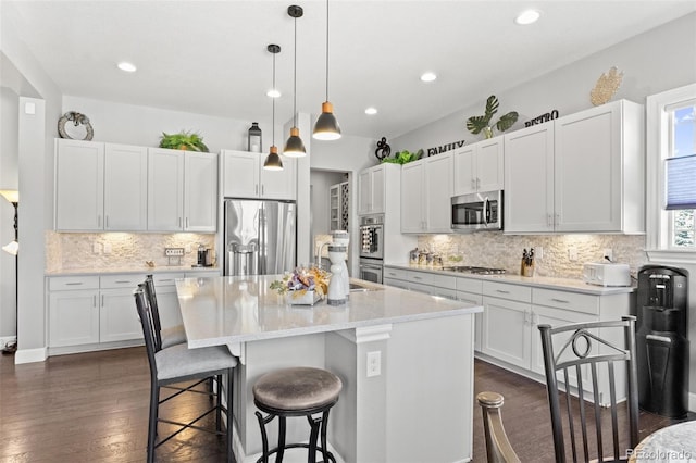 kitchen featuring appliances with stainless steel finishes, hanging light fixtures, white cabinetry, dark hardwood / wood-style floors, and a kitchen island with sink