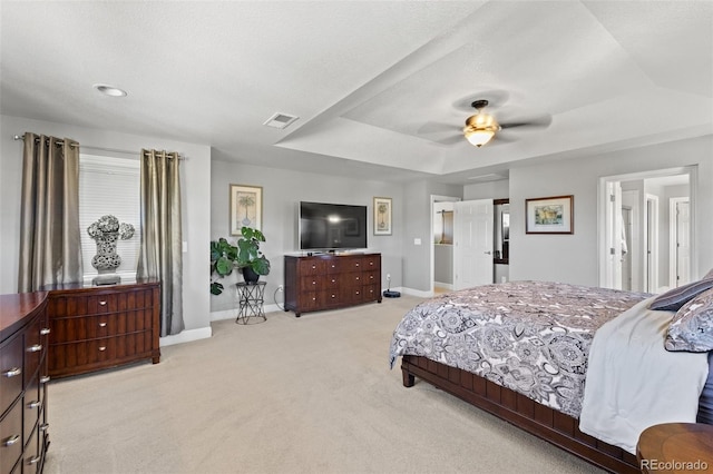 bedroom featuring a textured ceiling, light carpet, a tray ceiling, and ceiling fan