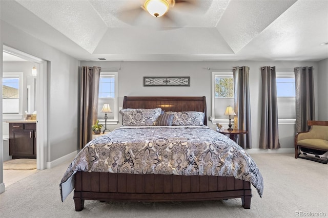 carpeted bedroom featuring multiple windows, ensuite bathroom, a tray ceiling, and ceiling fan