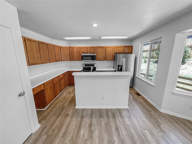19093 E Linvale Pl, Aurora, CO 80013 - kitchen featuring appliances with stainless steel finishes, light wood-style floors, light countertops, brown cabinetry, and a kitchen island