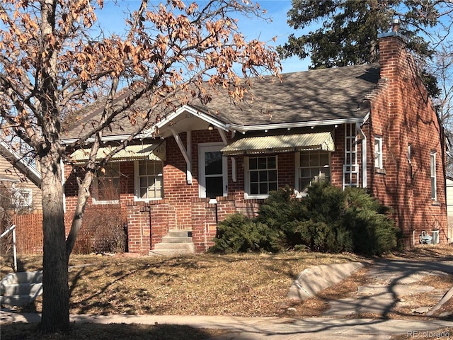 view of front of property featuring a shingled roof, brick siding, and a chimney