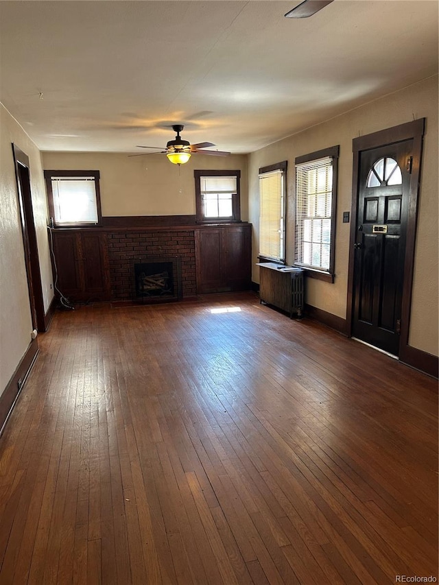 unfurnished living room with a ceiling fan, a brick fireplace, dark wood finished floors, and radiator heating unit