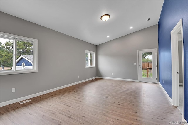 spare room with lofted ceiling, light wood-style flooring, visible vents, and baseboards