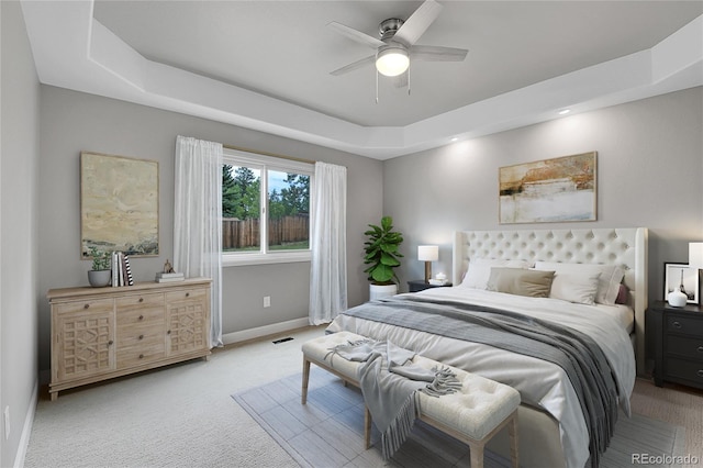 bedroom with visible vents, baseboards, a tray ceiling, light carpet, and a ceiling fan