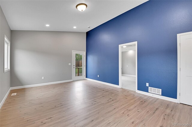 empty room featuring visible vents, lofted ceiling, baseboards, and wood finished floors