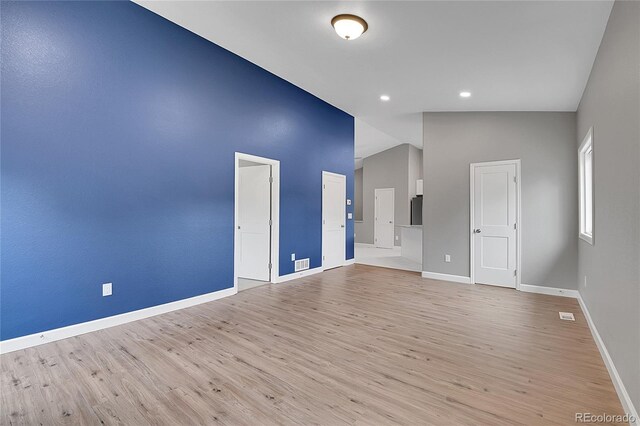 empty room featuring visible vents, baseboards, light wood-style floors, and vaulted ceiling