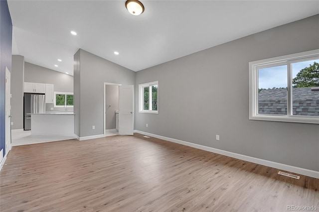 empty room with lofted ceiling, light wood-style flooring, baseboards, and visible vents