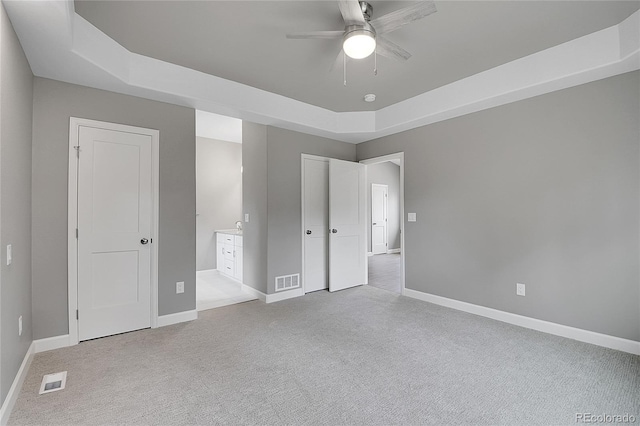 unfurnished bedroom with light carpet, visible vents, baseboards, and a tray ceiling