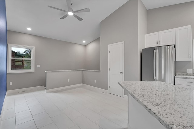 kitchen featuring light stone counters, white cabinetry, freestanding refrigerator, baseboards, and ceiling fan