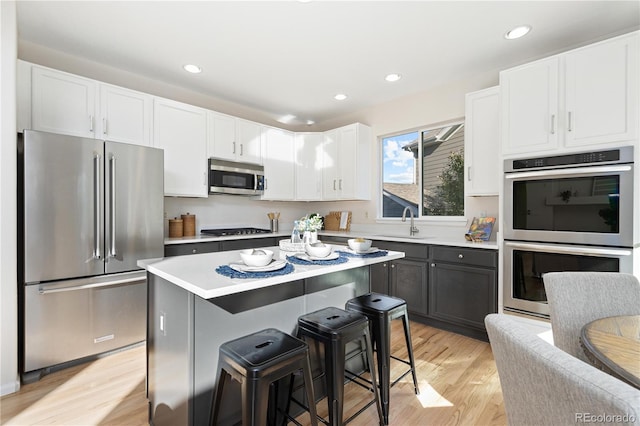 kitchen with white cabinetry, a center island, stainless steel appliances, light hardwood / wood-style flooring, and a kitchen bar