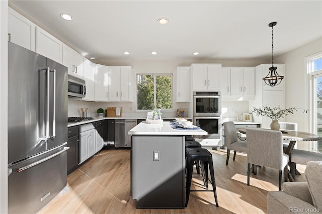 kitchen with a kitchen breakfast bar, stainless steel appliances, pendant lighting, white cabinets, and a center island