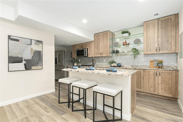 kitchen featuring decorative backsplash, stainless steel appliances, light hardwood / wood-style flooring, a kitchen island, and a breakfast bar area