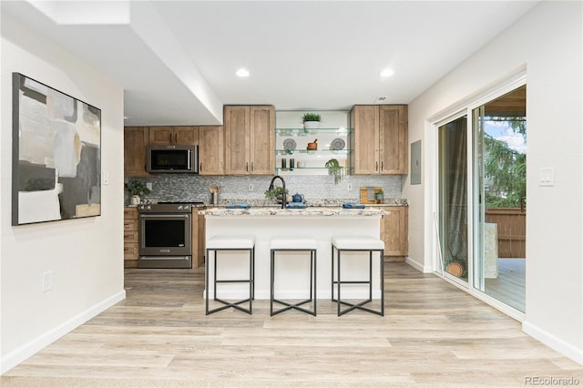 kitchen with a kitchen breakfast bar, light wood-type flooring, stainless steel appliances, and a center island with sink